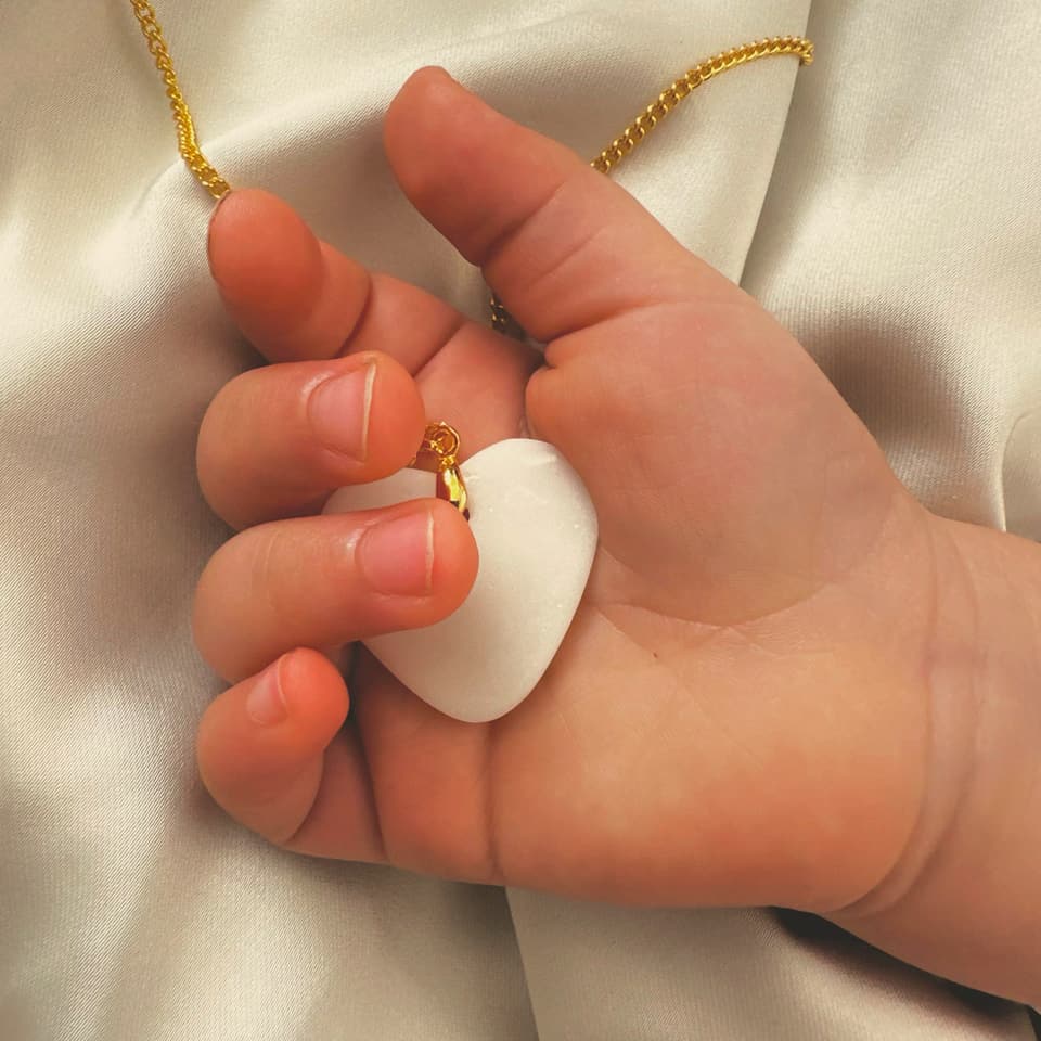Baby's tiny hand reaching toward a breast milk pendant