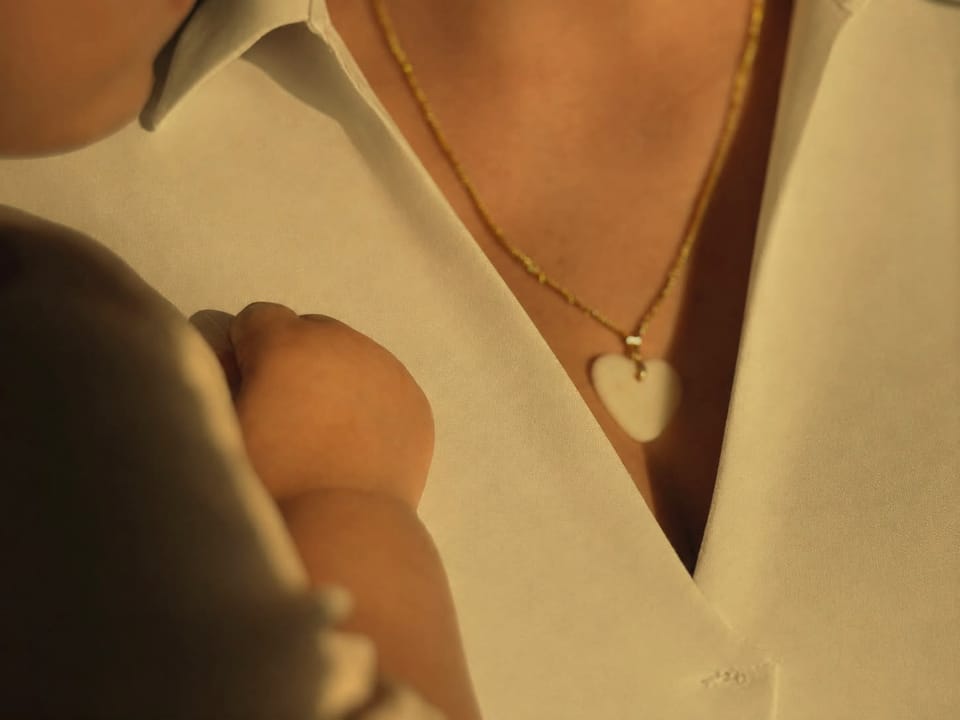 Mother holding her baby close, wearing a breast milk pendant necklace